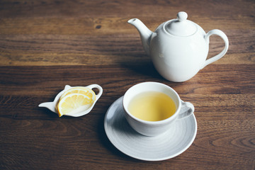 Close-up shoot of cup of hot tea with lemon and infusion teapot on brown wooden table. Boost your immune system naturally