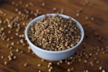 Buckwheat grain on ceramic bowl over wooden table.