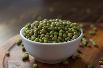 Organic mung beans on white ceramic bowl over wooden background.