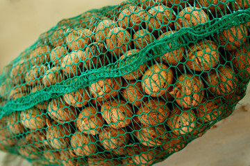 Background of bunch of unpeeled riped walnuts, collected into green wicker net bag