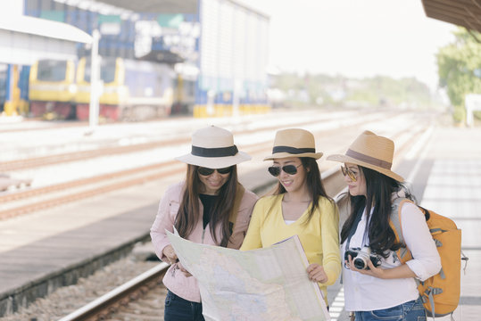 Group of beautiful traveler woman (friends) searching right direction at train station.Asian Backpackers pointing and planning holiday vacation with location map.