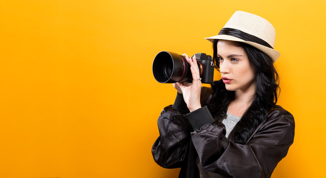  Young woman holding a camera on a yellow background