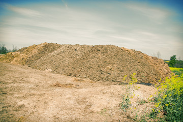 Pile of manure in the countryside with blue cloudy sky. Heap of dung in field on the farm yard with...
