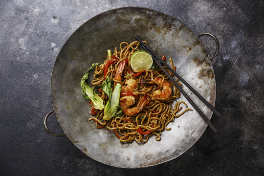 Udon noodles stir-fried with Tiger shrimps and vegetable in wok cooking pan on dark background