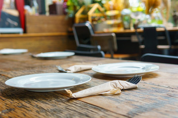 Side view. three white empty dish with cutlery on the old vintage wooden table with blurred cafe background..