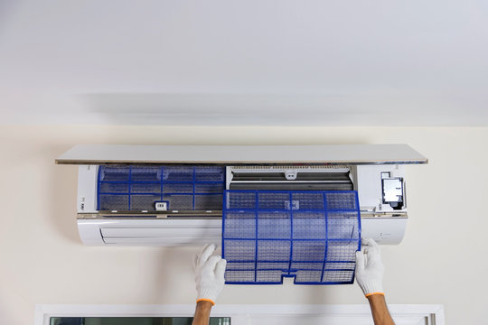 Man's hand is wearing a glove removing the air filter of the air conditioner for cleaning.