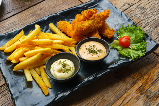fish and chips with salad cream and wasabi cream sauces in black ceramic dish on wooden table.