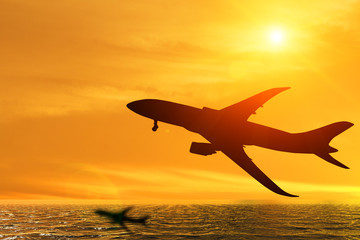 Fototapeta na wymiar Silhouette of airplane taking off flight with orange sky background over the ocean