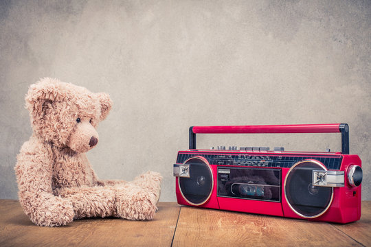 Retro Teddy Bear toy and red old outdated cassette radio recorder from 80s front concrete wall background. Listening music concept. Vintage style filtered photo