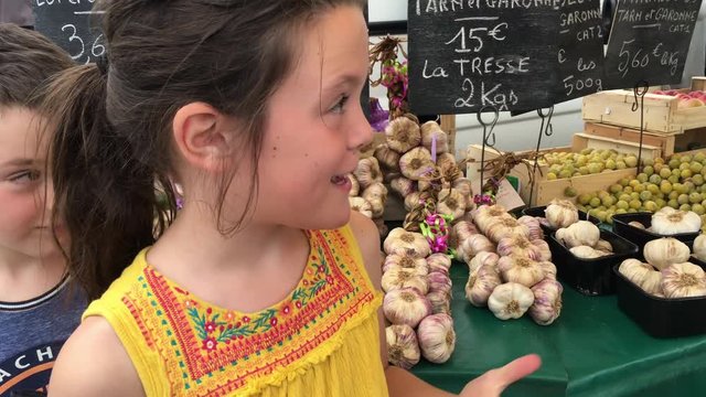 Girl and boy stand in a fresh farmers market in a French street market. Tourist shot with wild garlic behind them
