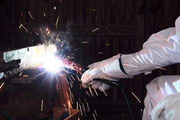 Hands of professional industrial welder with torch and protective gloves welding metal steel with spark in the factory.