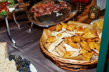Bascket with bread stands among dishes with snacks on grey table