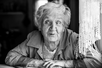 An elderly woman sitting at table in the house. Emotional black and white portraits.
