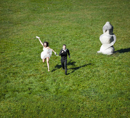 Obraz premium Look from above at happy wedding couple running across the green lawn