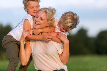 woman romps with her two sons on the grass