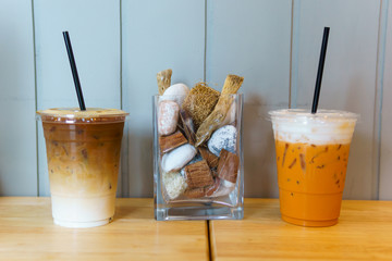 close up of iced latte coffee and thai tea in transparent plastic glass and straw on the wooden table. coffee and cafe decoration concept.