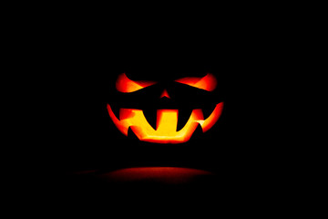 A very terrible Halloween pumpkin, with a terrible look and a smirk of a villain, in the dark