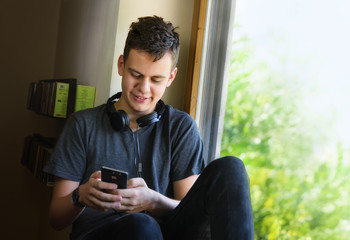 happy teenage boy sitting on window and using phone - 169731236