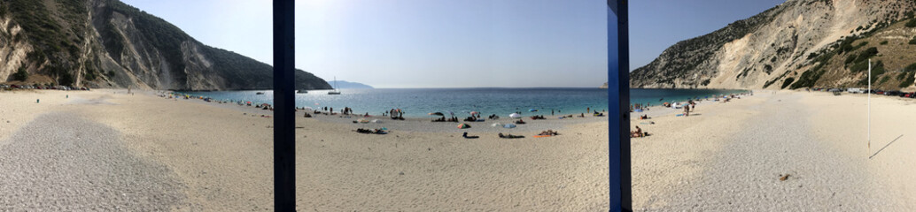 Panoramic view of Myrtos beach with its white sand, blue sea, many tourists and umbrellas, in Cephalonia or Kefalonia in Greece.