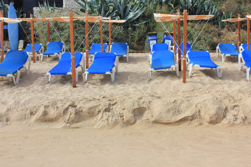 Beach lounge bed with umbrella to protect people from sun, on white sand beach. Tropical holiday banner background with empty copyspace. Travel, vacation, relax, tourism, sun bathing, tanning concept