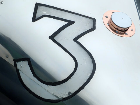 the number three painted on a vintage silver racing car with shiny copper fuel tank cover and rivets