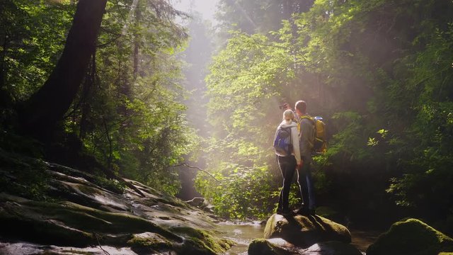 A pair of travelers are photographed in a picturesque place in a forest near a mountain river.