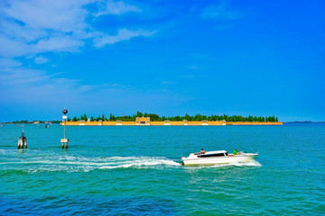 Fototapeta na wymiar View of Venetian Lagoon with a boat passing by on a sunny day in Venice.