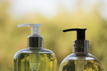 Close-up: two bottles of liquid soap or shampoo of green and yellow colors are on a blurred green background of nature. Concept: everyday personal care products.
