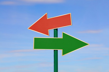 Road sign with two different arrows over blue sky