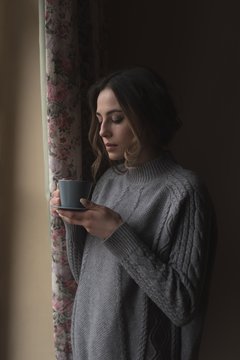 Woman Having Coffee While Standing By Window