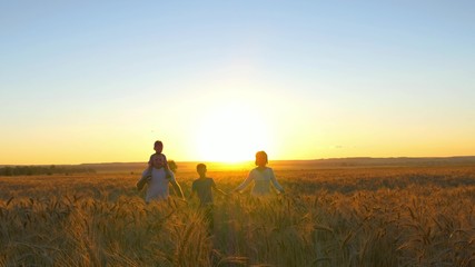 Happy family is walking along a wheat field on a sunset background
