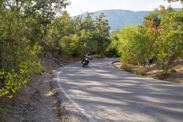 Young man riding a motorcycle on road turning in a curve in the mountains on sunny day. 