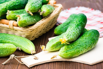 Fresh cucumbers on the cutting board and in a basket on a wooden table