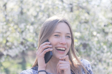 beautiful young womfn in spring park using cellphone and having fun, flower background 