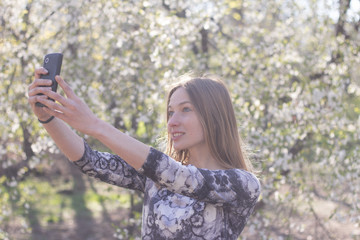 beautiful young womfn in spring park using cellphone and having fun, flower background 