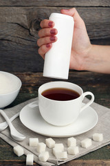 Female hand throwing sweetener tablets in cup of tea