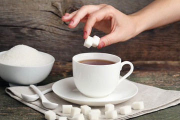 Fototapeta na wymiar Female hand throwing sugar cubes in cup of tea
