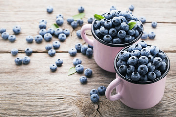 Ripe blueberries in pink mugs on wooden table