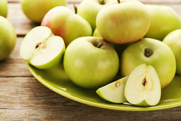 Ripe green apples in plate on wooden table