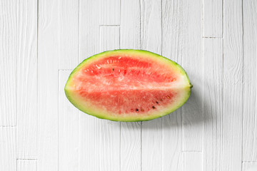Fototapeta na wymiar A quarter of a watermelon on white wood background top view. Piece of fresh watermelon on white table