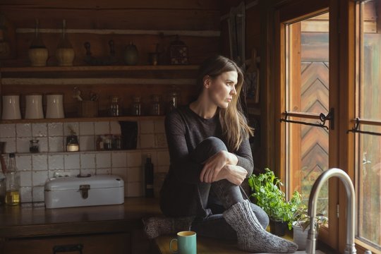 Thoughtful Woman Looking Through Window In Kitchen