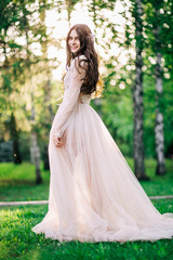 beautiful young girl bride brunette in delicate Bridal boudoir gown of lace and tulle in beige color is outdoors, in trees, birches, profile