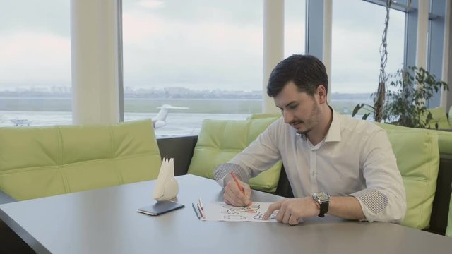 Businessman paints coloring book in airport during waiting boarding on plane