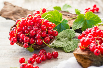 Red currant in a bowl, berries and leaves scattered on a shabby wood
