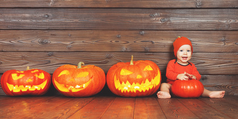happy baby in costume for Halloween with pumpkins on wooden background