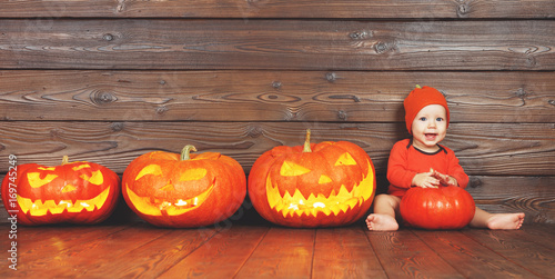 happy baby in costume for Halloween with pumpkins on wooden background