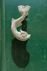 Close-up view of the fish shaped knocker on a green wooden door