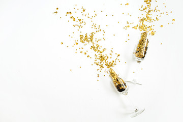 Champagne glasses with golden confetti tinsel on white background. Flat lay, top view celebrate...