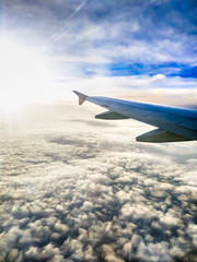 Aerial view of soft clouds and airplane wing on sunrise through an aircraft window. Plane flight. Beautiful sky, cloudscape and horizon.