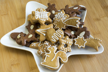 Many kinds of Christmas cookies on white plate, gingerbread dark and light, star shape dish, bamboo wooden background